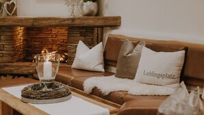 A cozy living room with a fireplace, a glass candle holder, and a couch with a 'Lieblingsplatz' pillow. - B&B Hotel Die Bergquelle (Flachau)