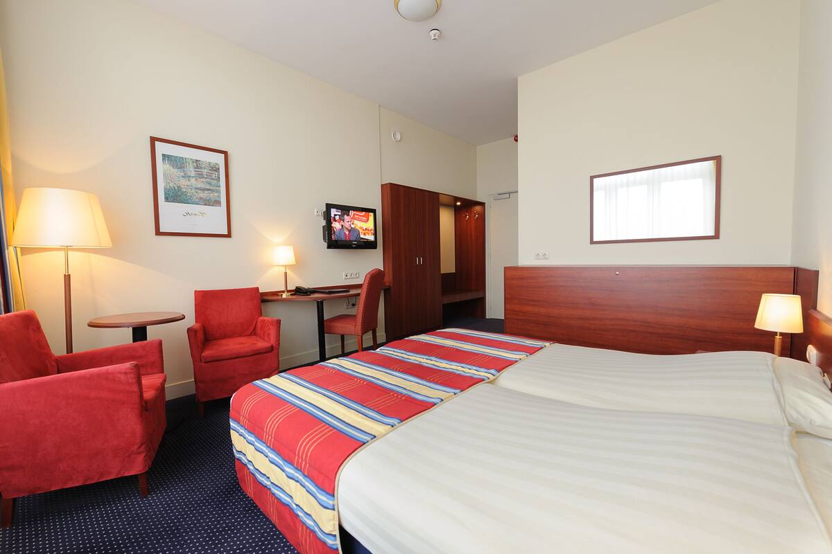 A hotel room with a bed, a desk, a chair, a TV, and a wardrobe.