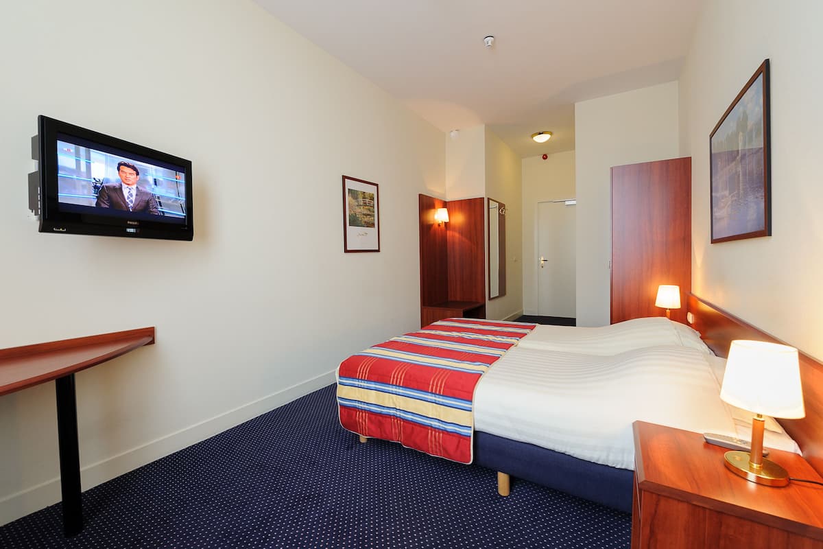 A hotel room with a bed, a desk, a TV, a lamp, and a door.