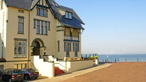 Ett stort hotell med en balkong som vetter mot havet, och en trappa som leder till entrén.