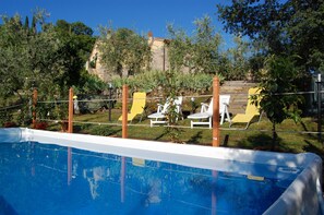 Ein Swimmingpool mit weißen Liegestühlen und ein Steinhaus im Hintergrund.