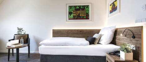 Une chambre à coucher moderne avec un grand lit, une petite table, une chaise et des œuvres d’art accrochées aux murs.