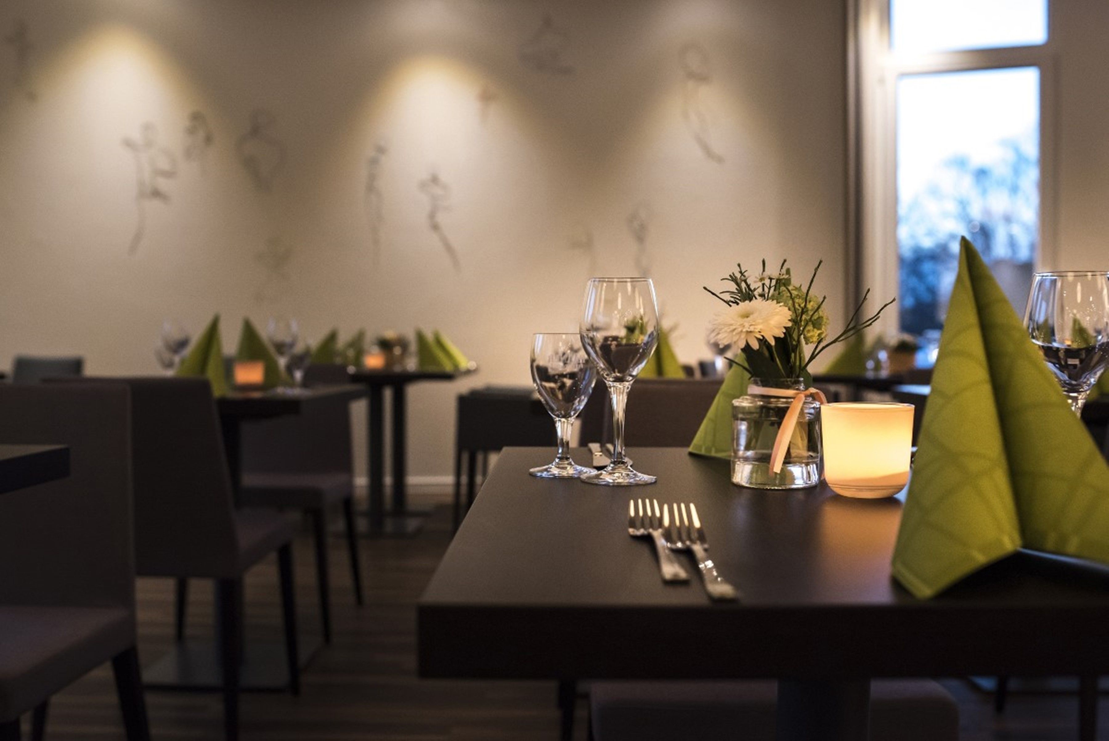 A dining table set with wine glasses, a candle, and a flower arrangement.