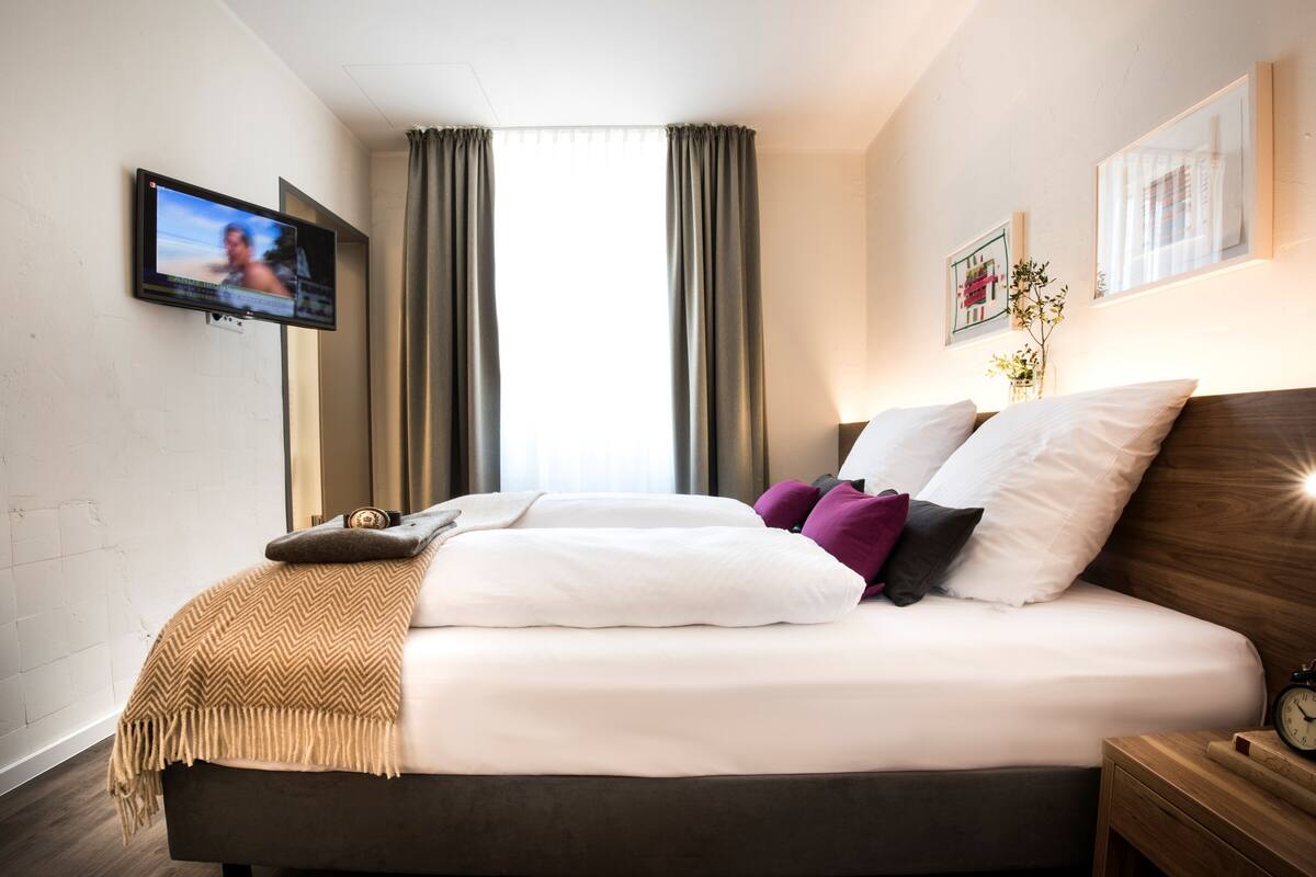 Ein modernes Hotelzimmer mit einem großen Bett, einem Wandfernseher und einem Fenster mit Vorhängen.