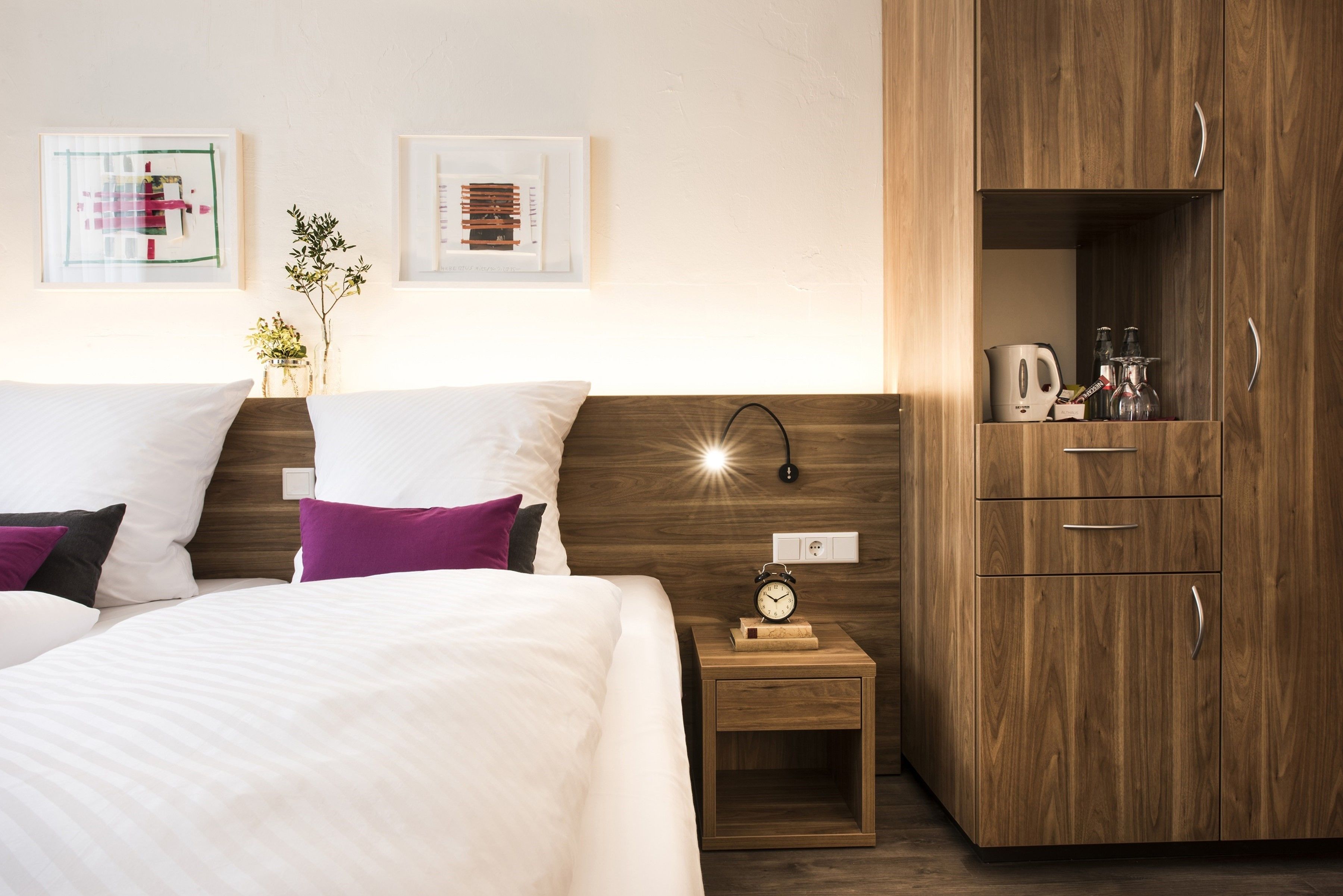 A neatly arranged hotel room with a bed, bedside table, and a wooden wardrobe.