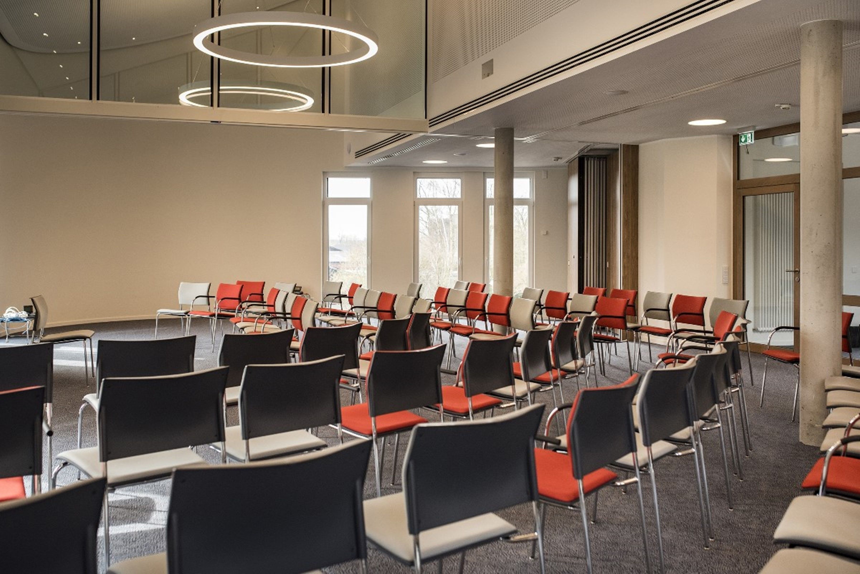 Un salón de conferencias con filas de sillas, ventanas amplias y un diseño moderno de techo.