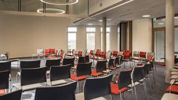 Un salón de conferencias con filas de sillas, ventanas amplias y un diseño moderno de techo.