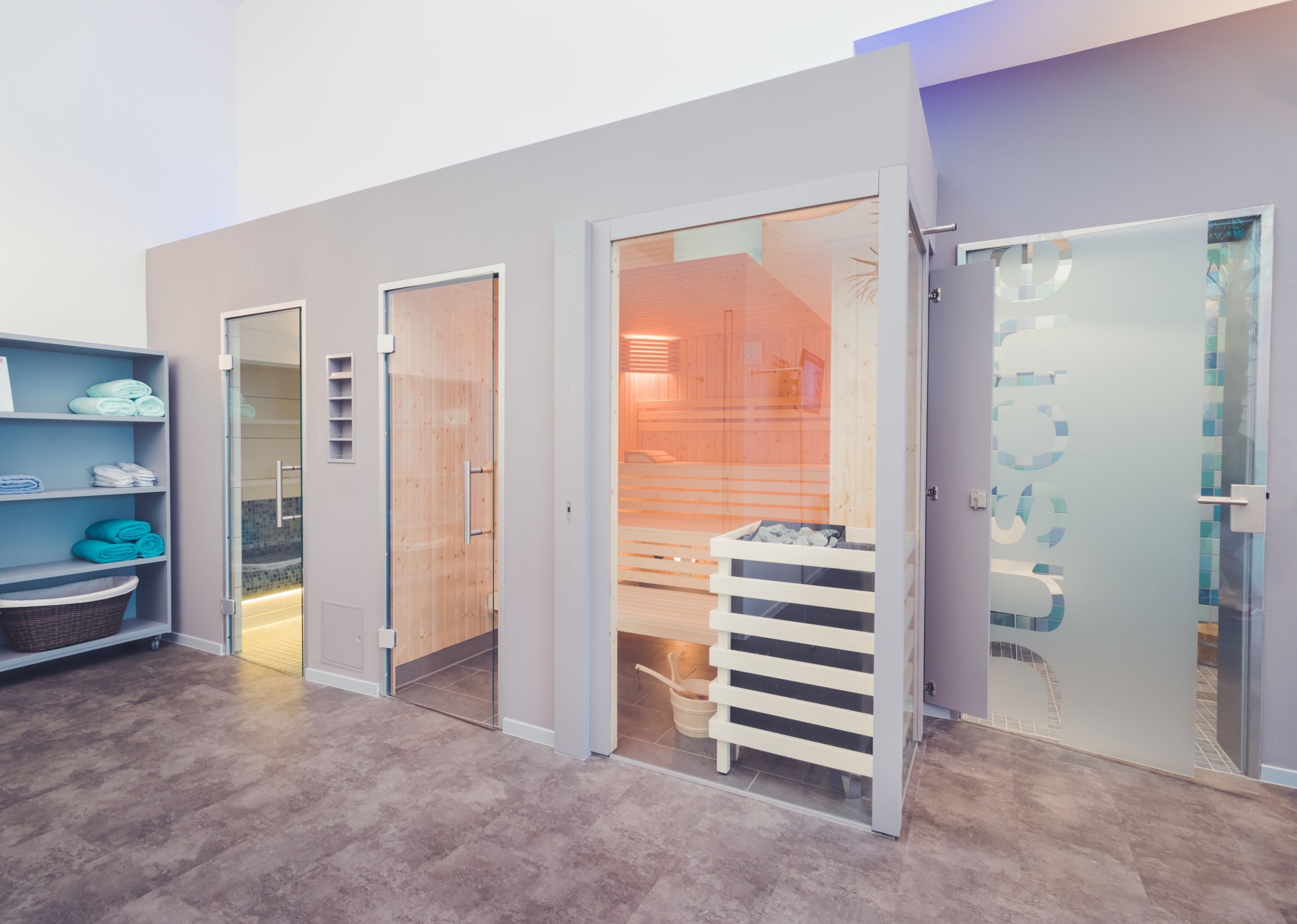 Ein modernes Interieur mit einer Glastür, die in einen Raum mit Holzeinrichtung führt, einem Regal mit gefalteten Handtüchern und einem Korb auf dem Boden.