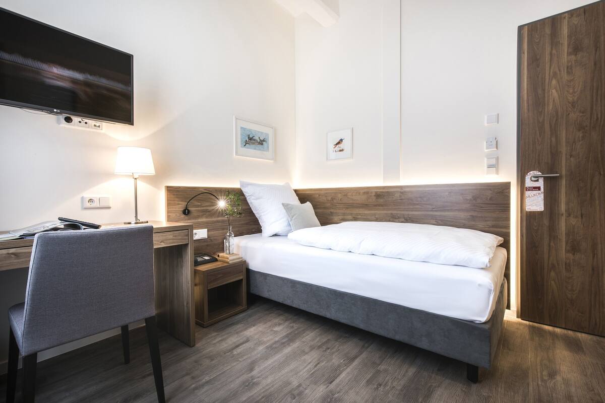 Ein modernes Hotelzimmer mit Bett, Schreibtisch, Stuhl und einem an der Wand befestigten Fernseher.