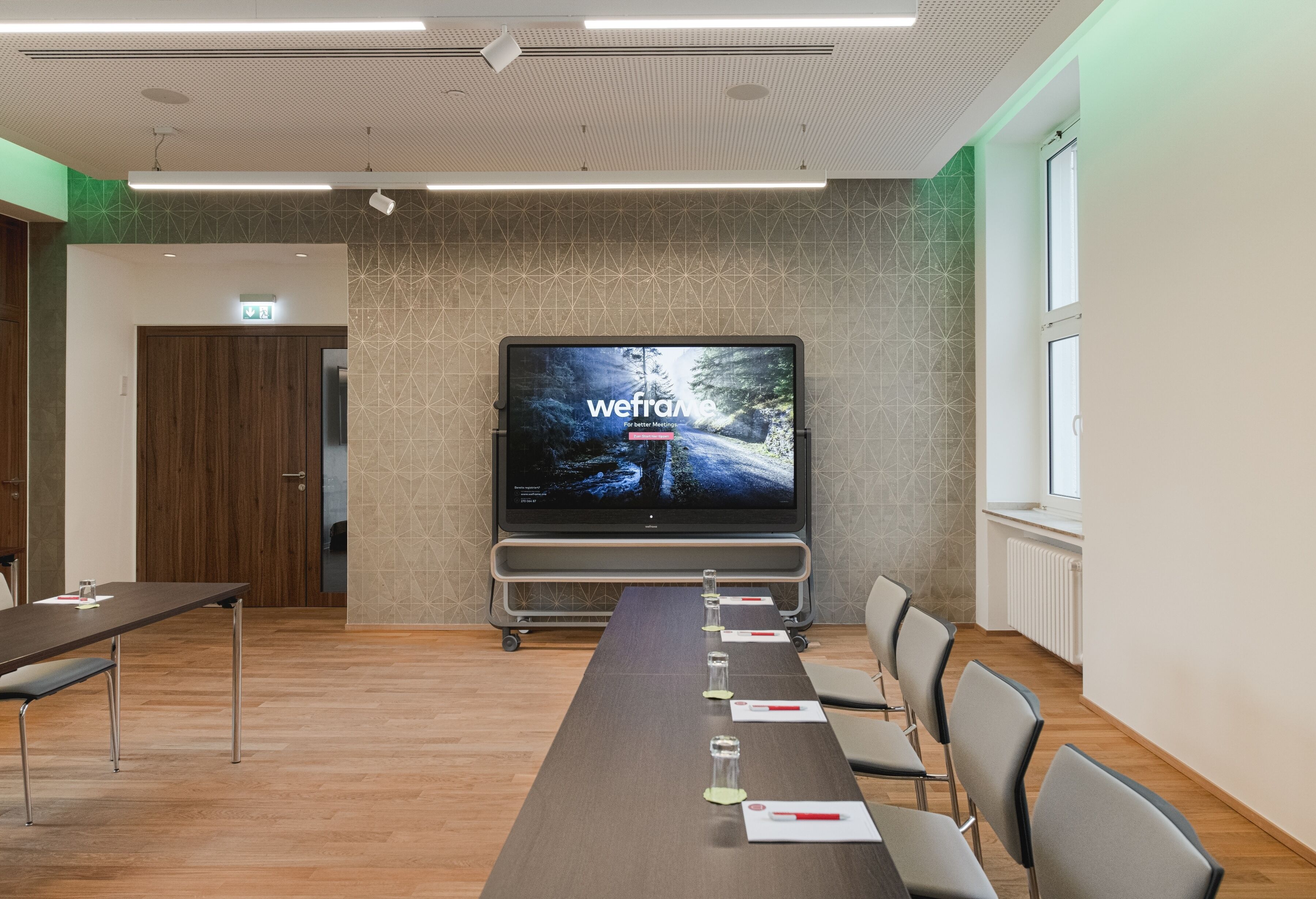 Uma sala de conferência com uma mesa comprida, cadeiras, uma tela de projetor e uma televisão exibindo 'wefra'.
