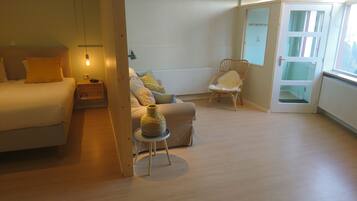 Un dormitorio con una cama, una silla, una mesita y una lámpara.