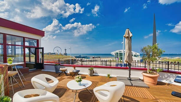 Une terrasse avec des sièges extérieurs, d’où l’on peut admirer la plage et une grande roue.