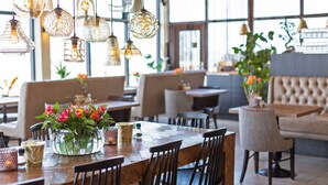L’intérieur d’un restaurant avec des tables et des chaises en bois, des lampes suspendues et un vase de fleurs posé sur la table.