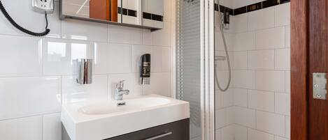 A modern bathroom with a white sink, dark cabinet, and a glass shower enclosure.