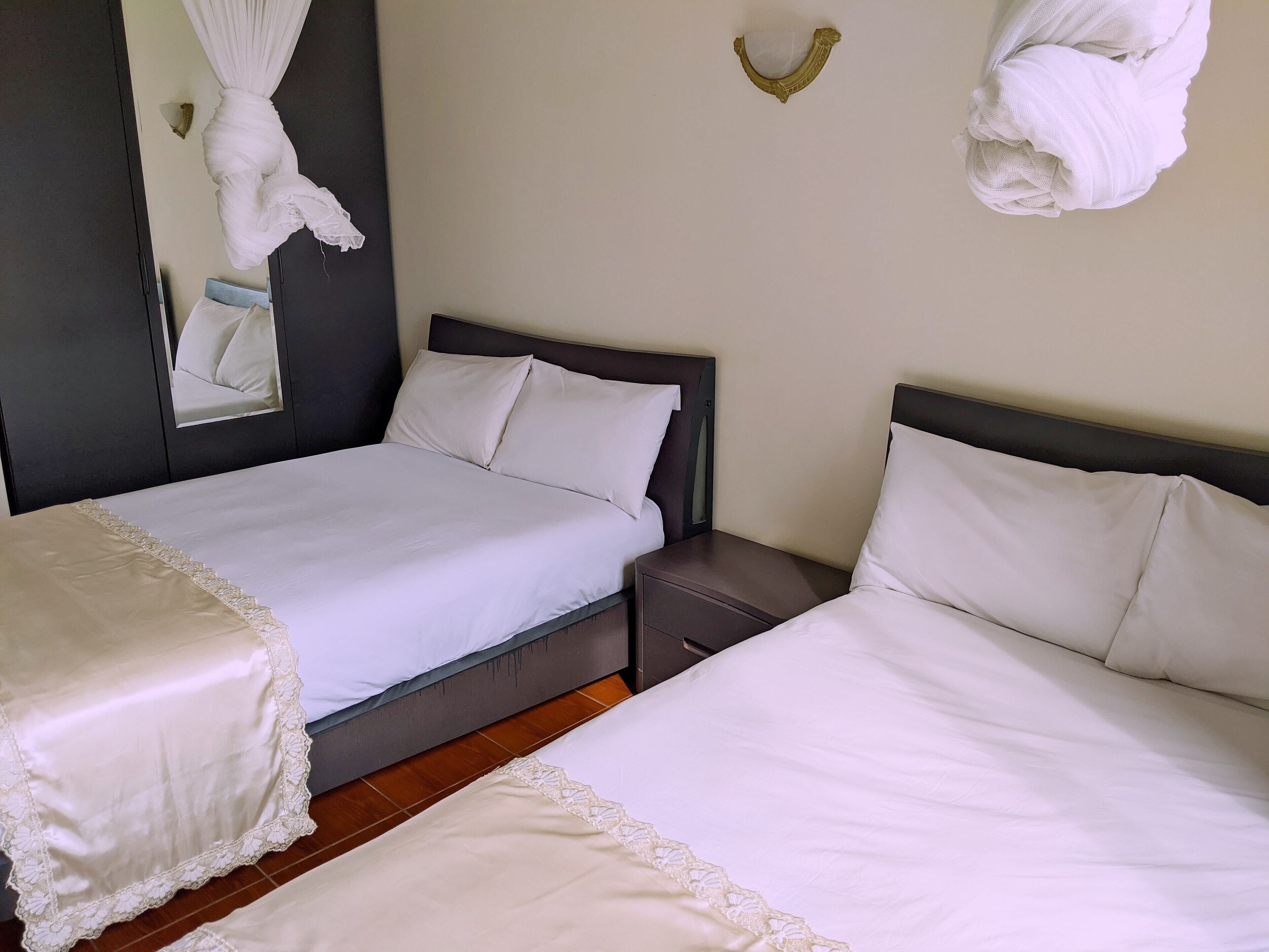Een hotelkamer met twee bedden, een donker hoofdeinde, een klein nachtkastje en een handdoekhouder aan de muur.
