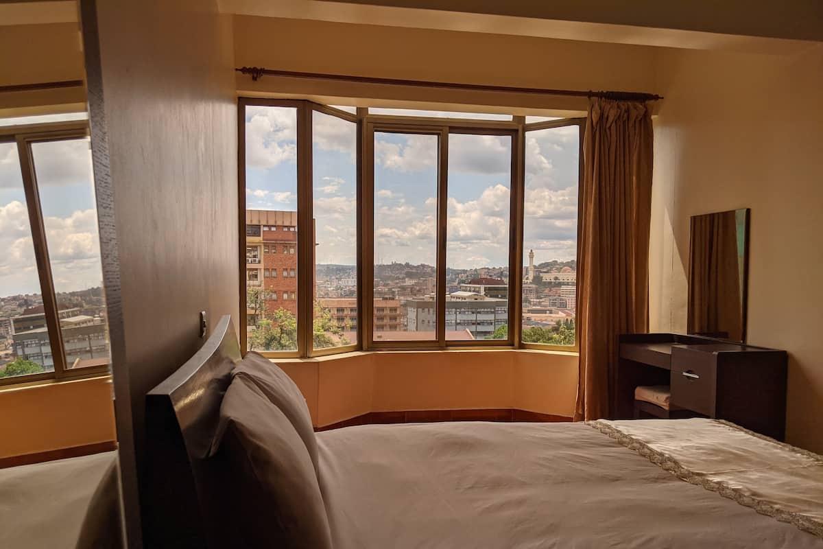 Habitación de hotel con un ventanal grande que ofrece vistas a la ciudad, una cama, un aparador y un espejo.