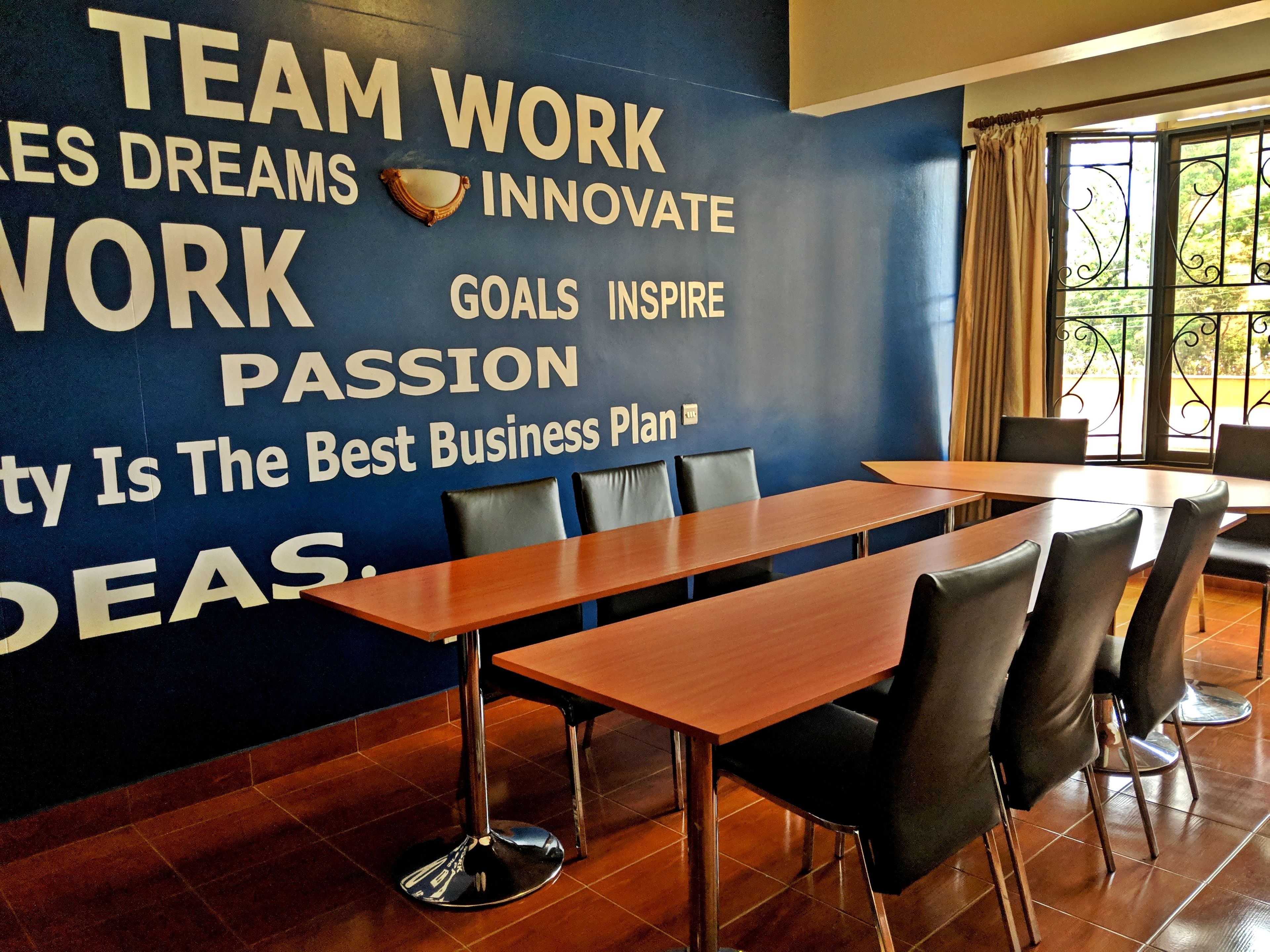 Une salle de conférence avec un grand poster motivant accroché au mur, des tables en bois et des chaises noires.