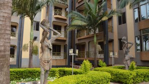Une cour ornée de statues, de palmiers et d’un bâtiment doté de balcons.