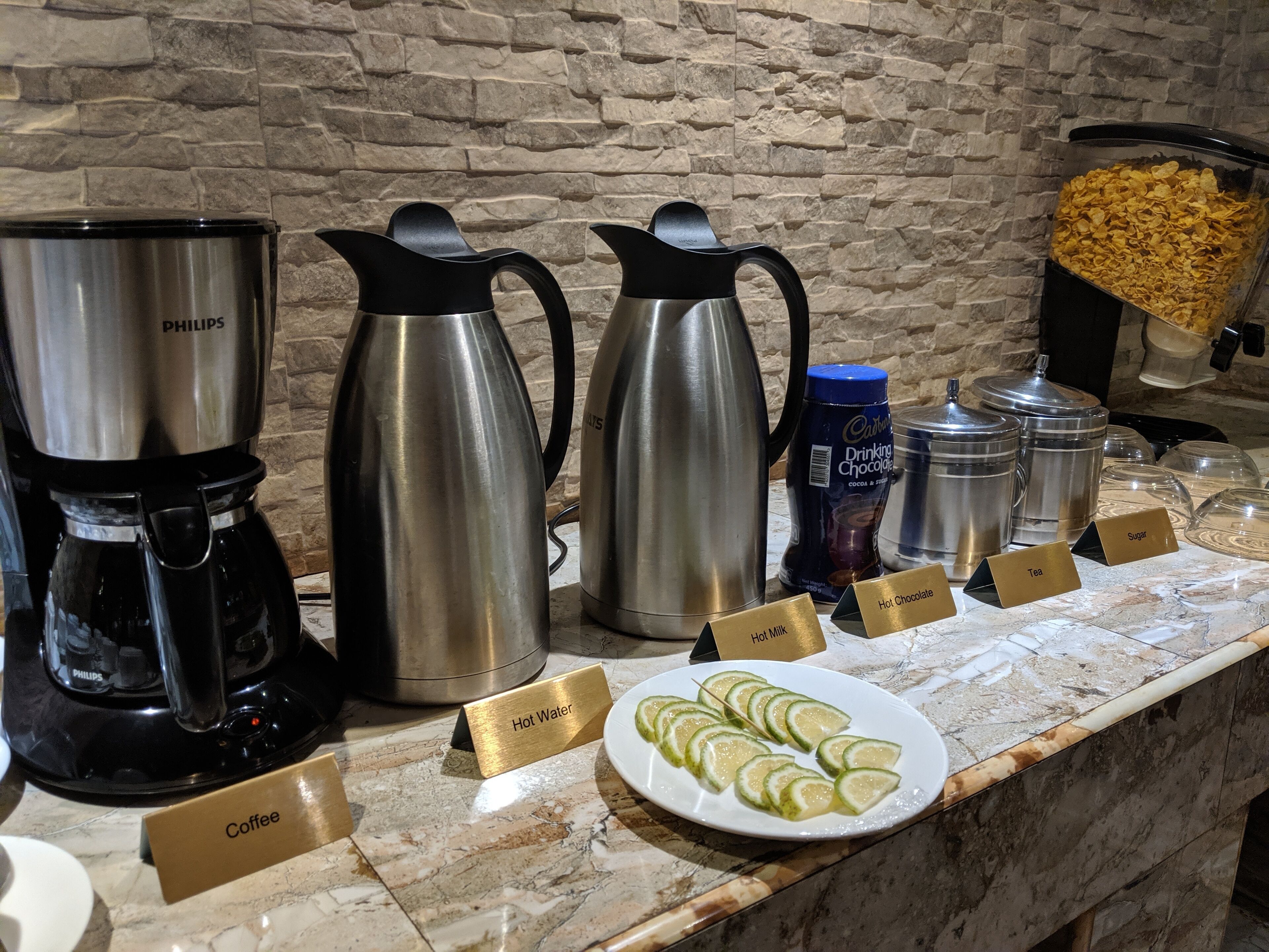 A buffet setup with coffee, tea, hot water, hot chocolate, sugar, and cocoa & chocolate containers.
