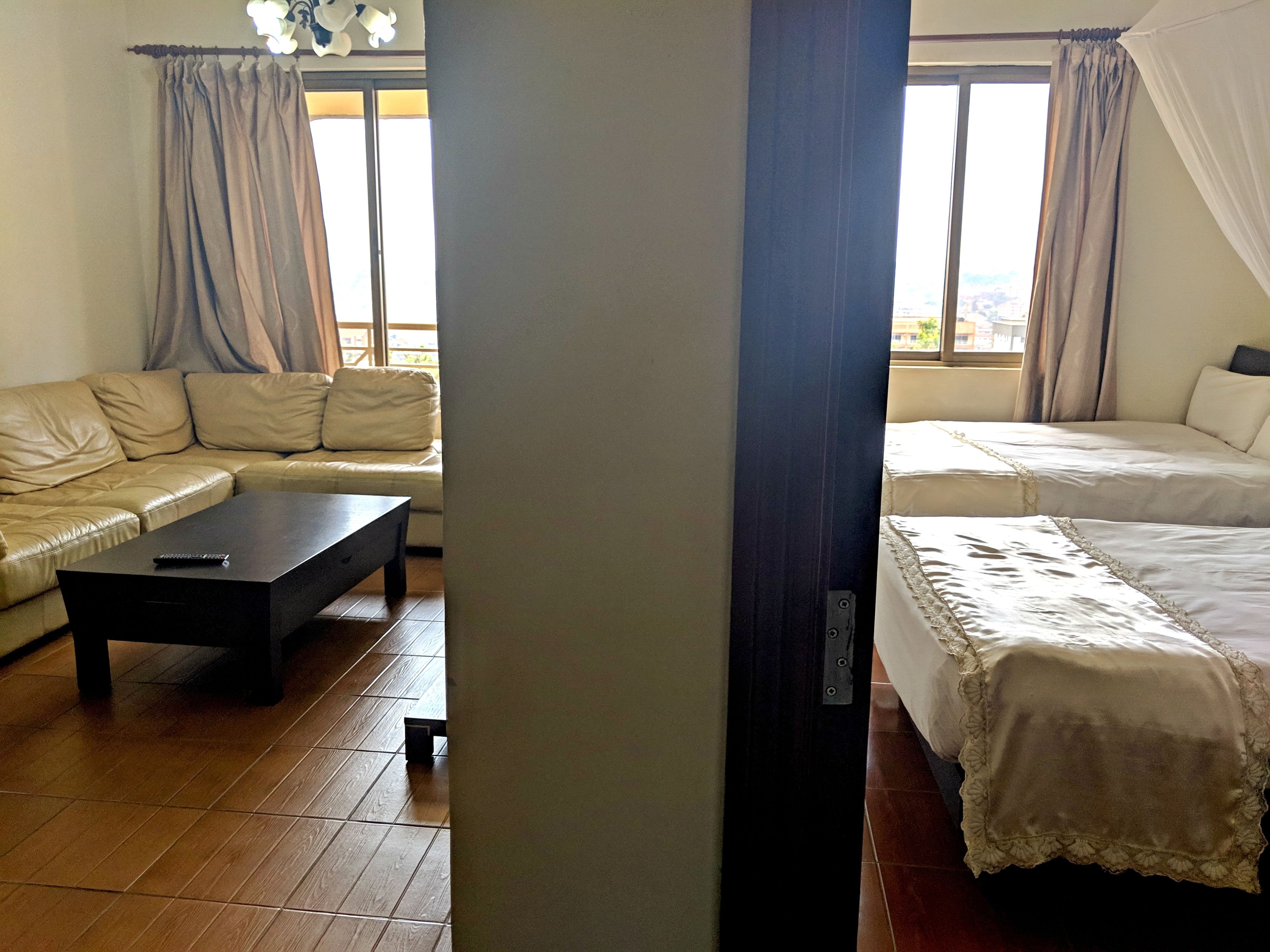 Una habitación con sofá, cama, mesa de centro y un amplio ventanal con cortinas.