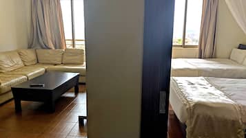 Una habitación con sofá, cama, mesa de centro y un amplio ventanal con cortinas.