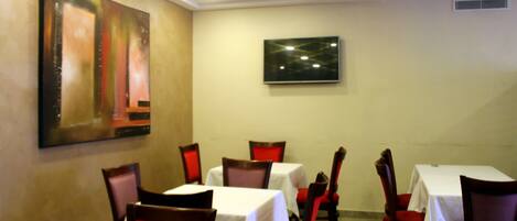A dining area with tables and chairs, a painting on the wall, and a television.