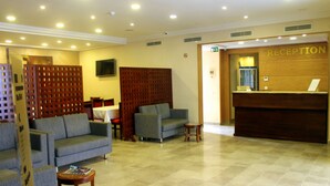 A hotel reception area with a reception desk, two sofas, a small table, and a TV mounted on the wall. - Résidence Le Consul (Tunis)