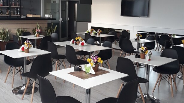 A modern dining area with multiple tables and chairs, a kitchen in the background, and a flat-screen TV mounted on the wall. - Victoria Hotel (Castello di Cisterna)