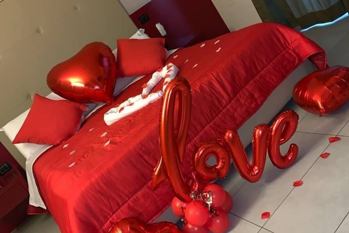 A bed with red bedding and heart-shaped balloons, including the word "love".