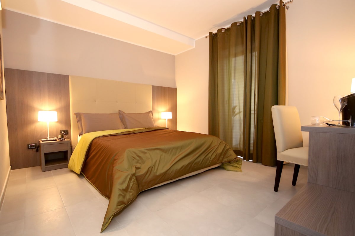 A hotel room with a bed, bedside lamps, a desk with a chair, and a mirror.