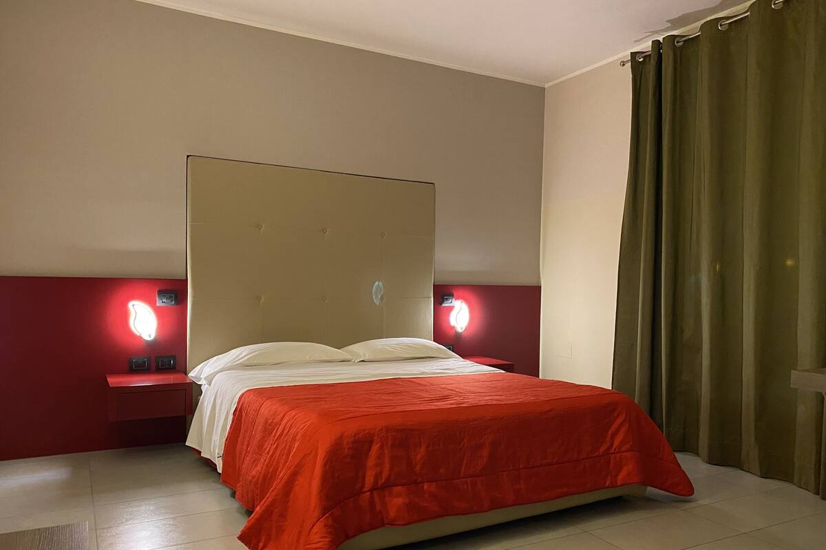 A hotel room with a large bed, red curtains, and two bedside lamps.
