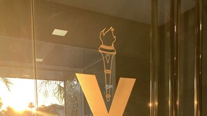A glass door with a large illuminated 'V' sign and a torch symbol above it. - Victoria Hotel (Castello di Cisterna)