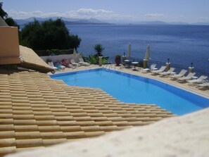 A pool with a view of the sea and mountains, surrounded by lounge chairs and umbrellas. - Oceanis Rooms Apartments (Corfu)