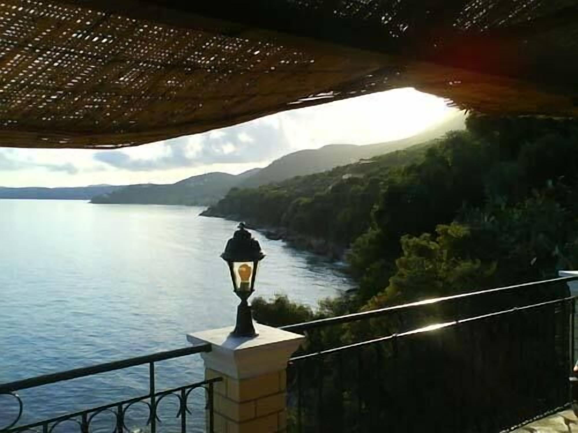 A balcony with a view of a calm sea and distant mountains.