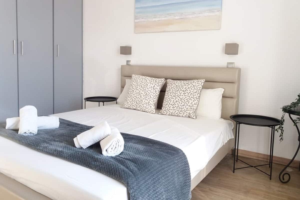 A bedroom with a bed, two bedside tables, a headboard, and a painting of a beach.