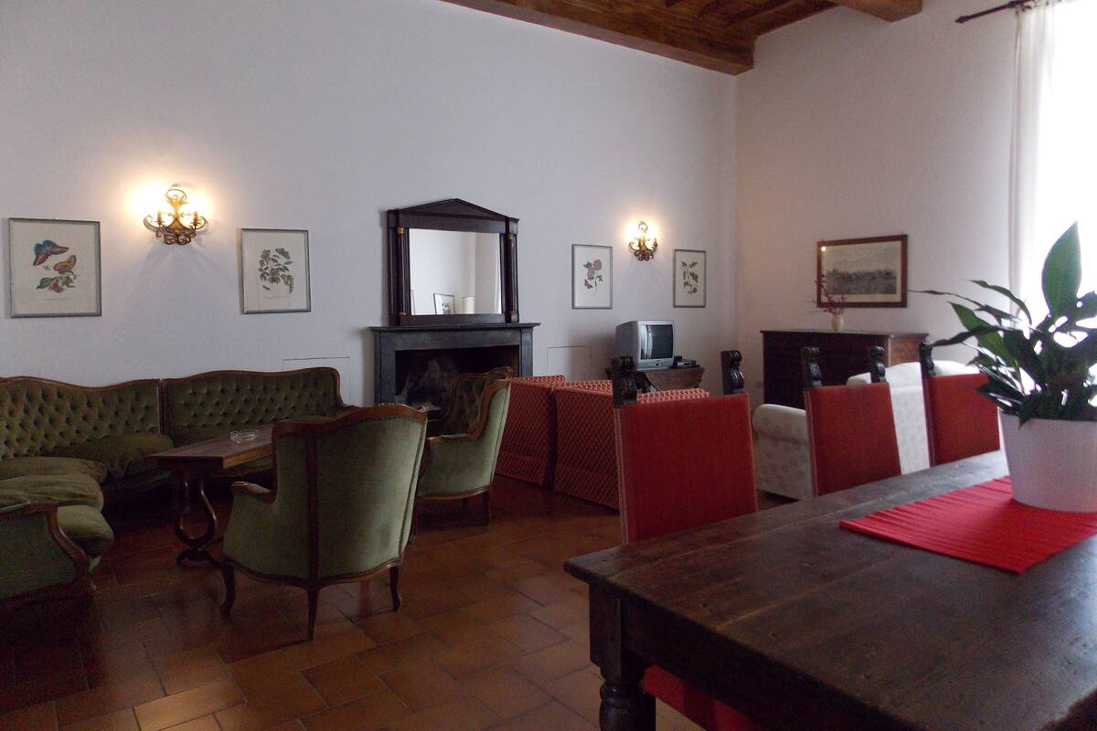 Ein traditionelles Wohnzimmer mit Kamin, einem grünen Polstersofa, roten Sesseln und gerahmten Kunstwerken an den Wänden.