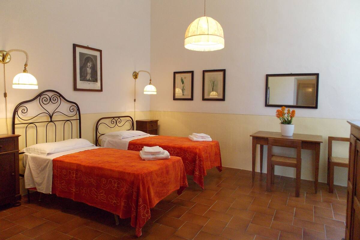 Ein Hotelzimmer mit zwei Betten, einem Schreibtisch, einem Stuhl, einem Spiegel und gerahmten Bildern an der Wand.