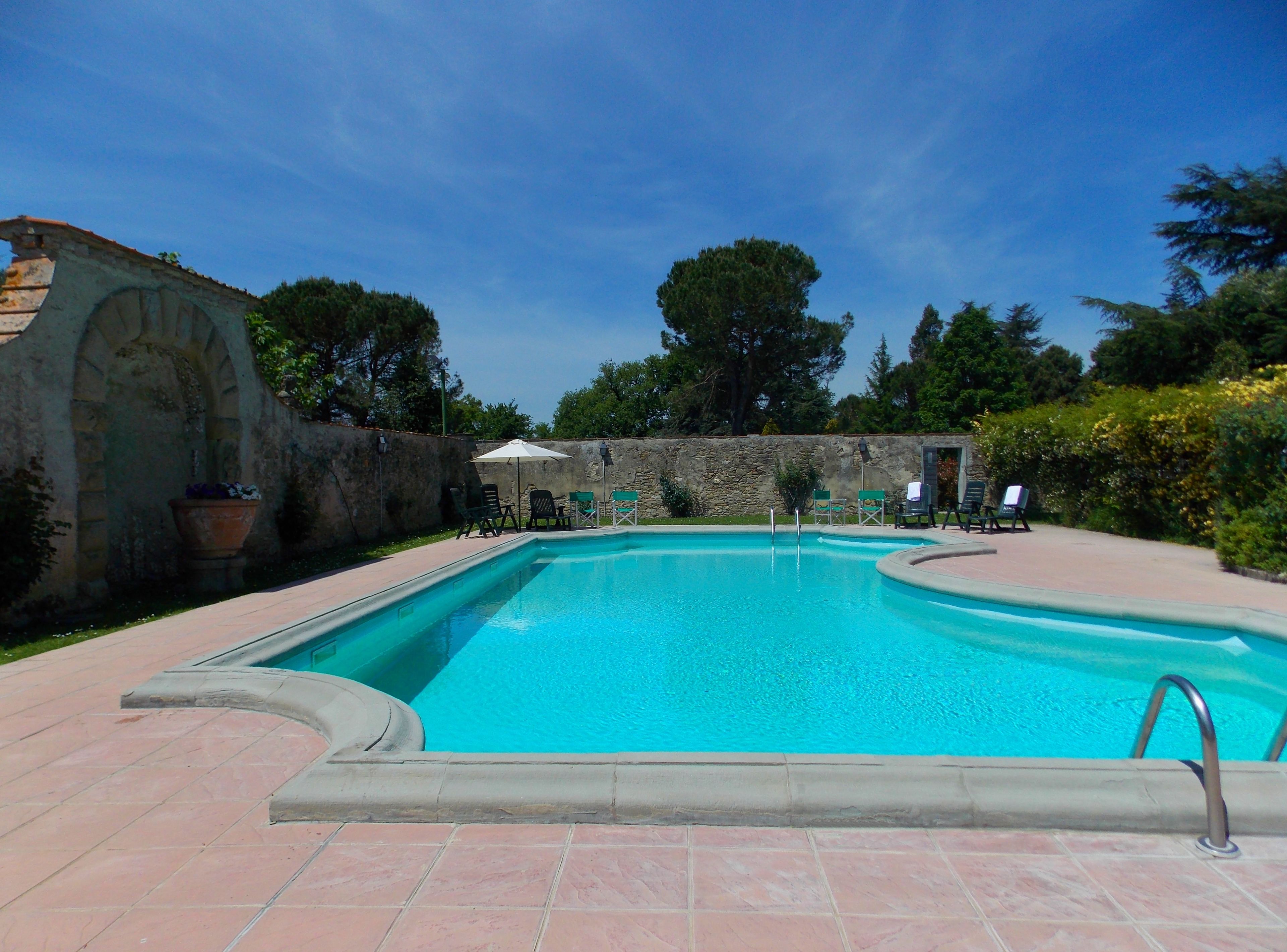 A rectangular swimming pool with a stone wall and a tiled deck surrounding it.
