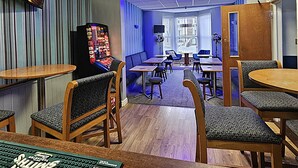 A room with a jukebox, tables, chairs, and a TV on the wall. - Denville Hotel (Blackpool)