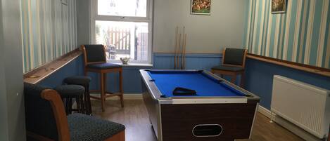 A pool table in a room with striped walls, a window, and two chairs.