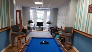 A pool table in a room with striped wallpaper, two sofas, and a television. - Denville Hotel (Blackpool)