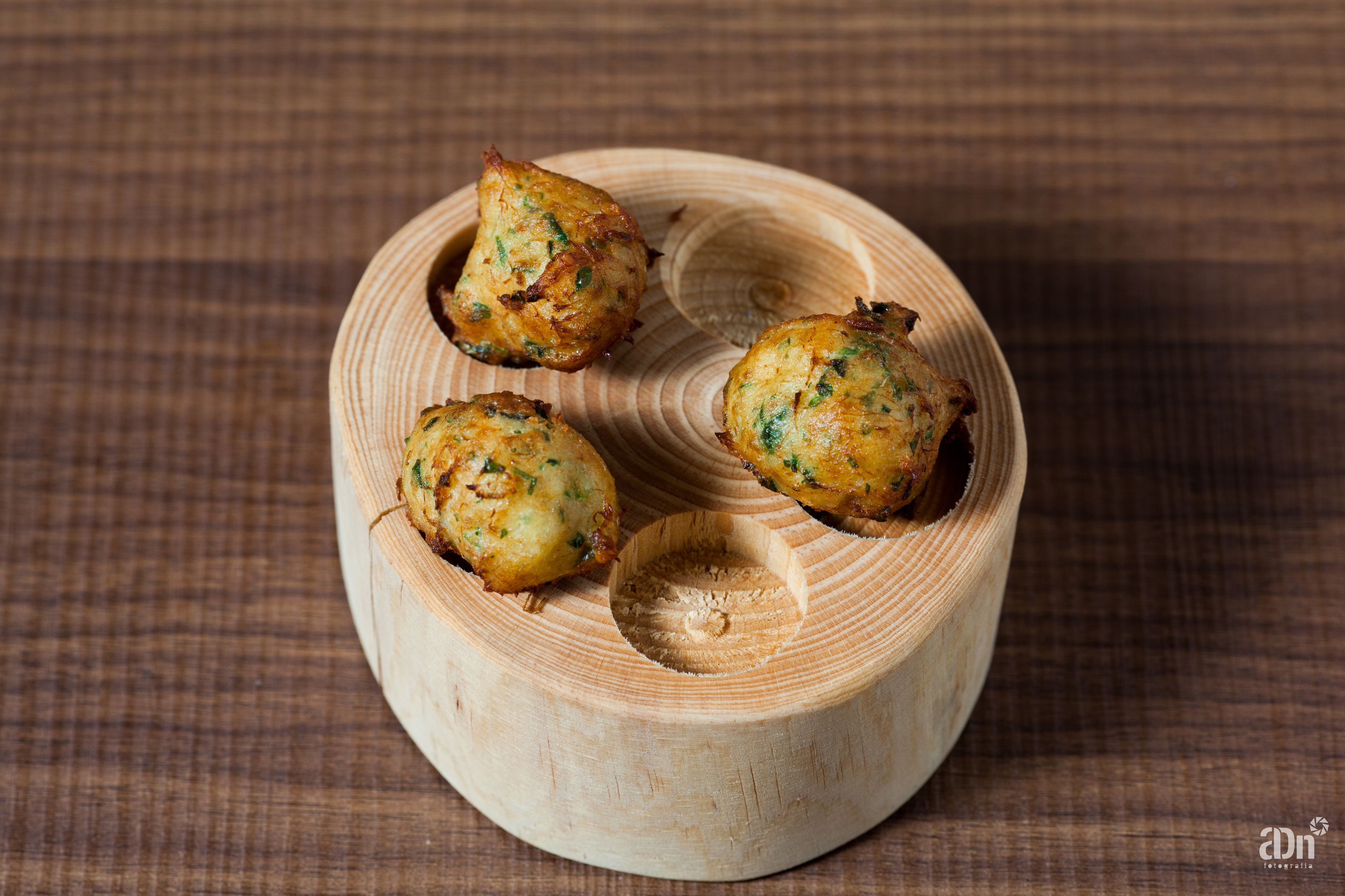 Three round, golden-brown food items on a wooden plate with a circular cutout.