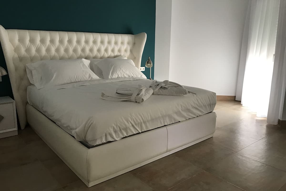 Un grand lit avec une tête de lit capitonnée, du linge de lit blanc et une serviette pliée posée sur le lit.
