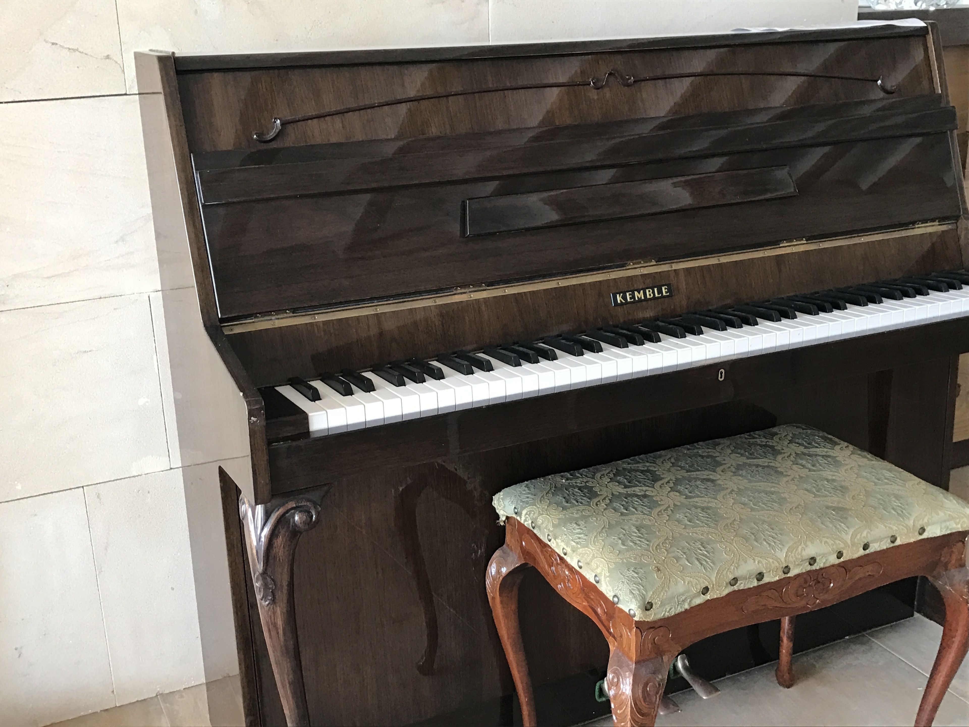 Un pianoforte a coda con una panca, appoggiato su una parete piastrellata.