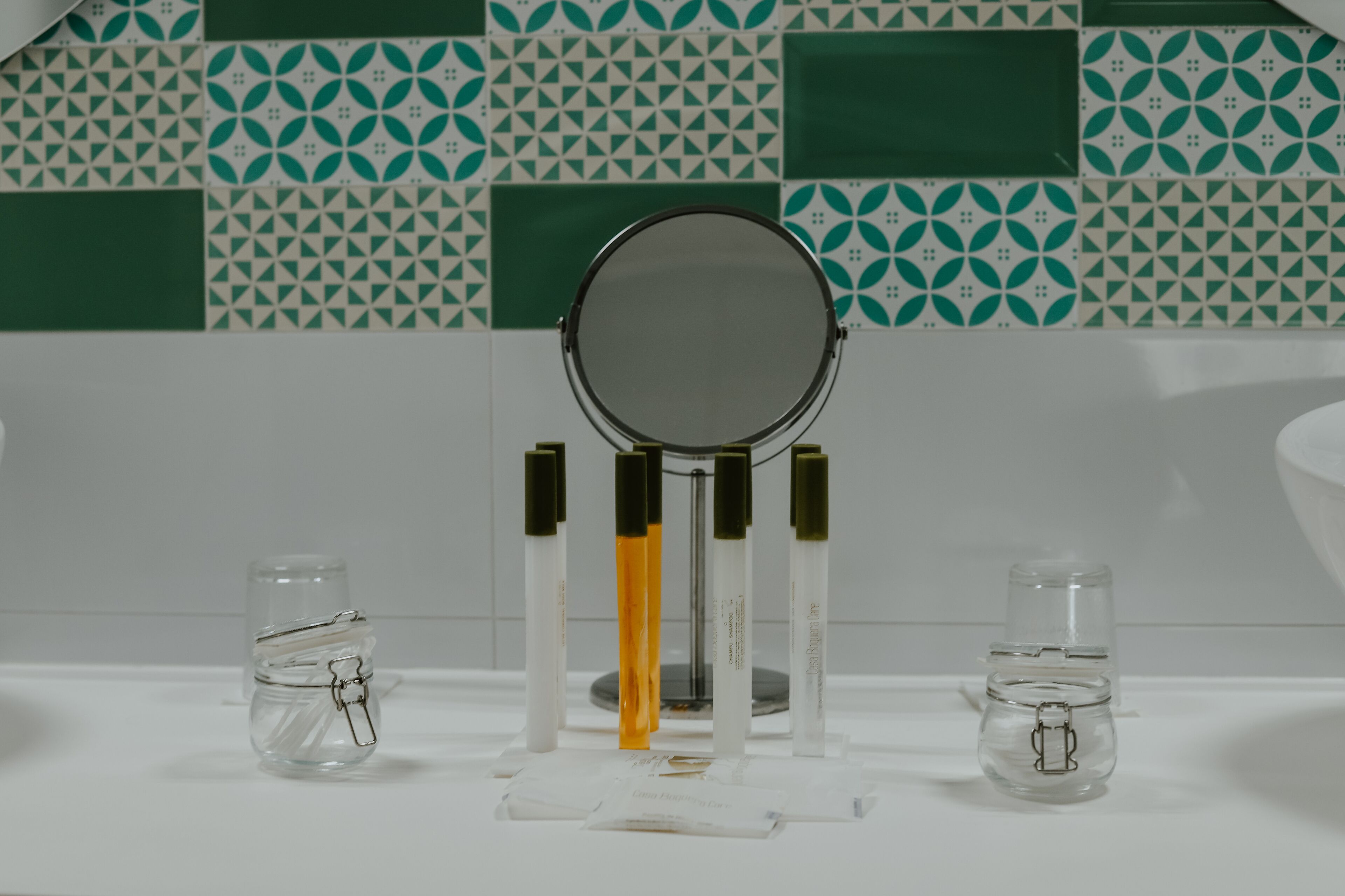 Une salle de bain avec un miroir, deux petits flacons et un lavabo blanc.
