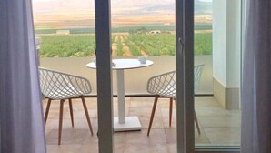 Un balcón con mesa y sillas, con vistas a un viñedo y montañas lejanas.