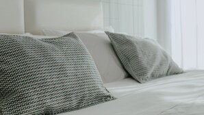Una cama bien tendida con sábanas blancas y dos almohadas estampadas.