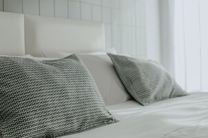 A neatly made bed with white linens and two patterned pillows.
