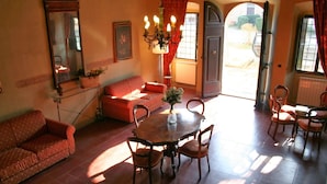 Una sala de estar acogedora con sofá, mesa de comedor, sillas, una araña y vistas a través de un ventanal abierto.