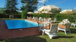 Una piscina con sillas de descanso y sombrillas, rodeada de follaje y árboles.